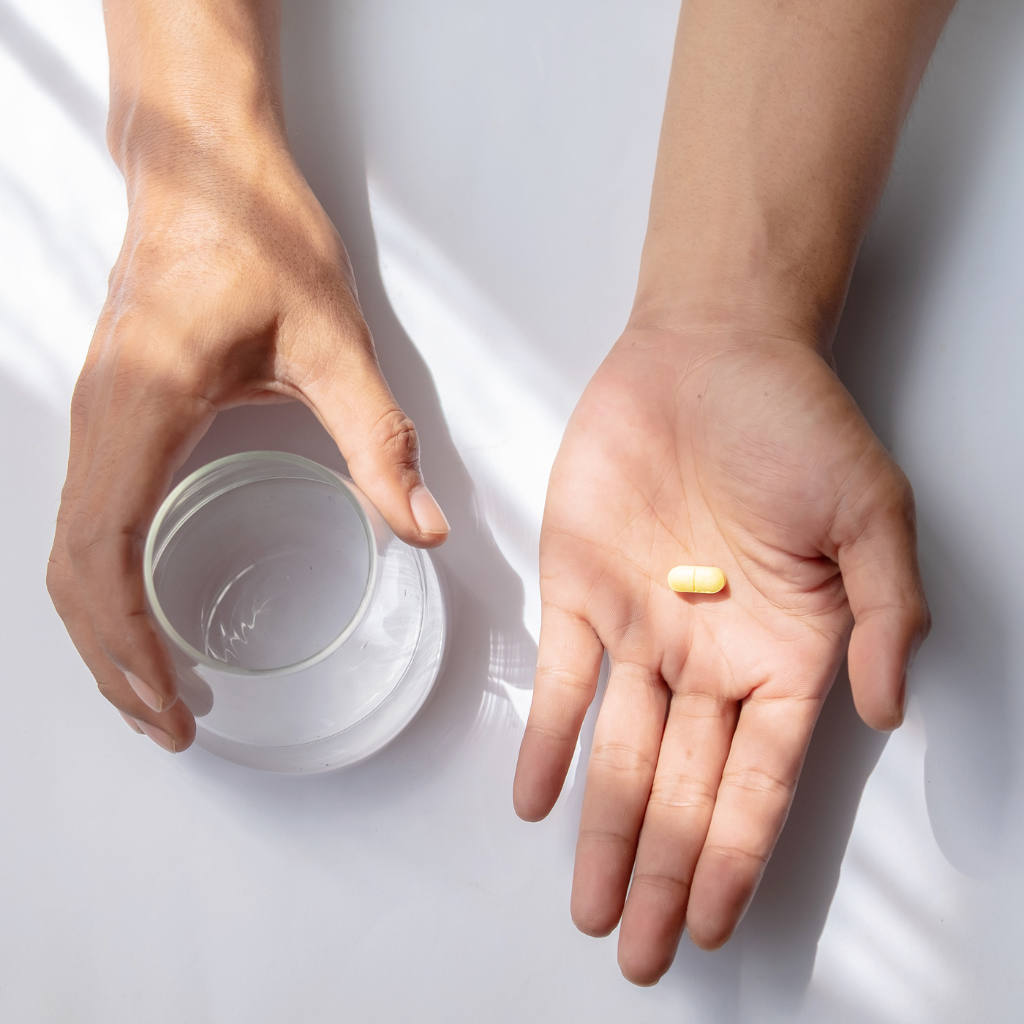 Deux mains tenant un verre d’eau et un comprimé